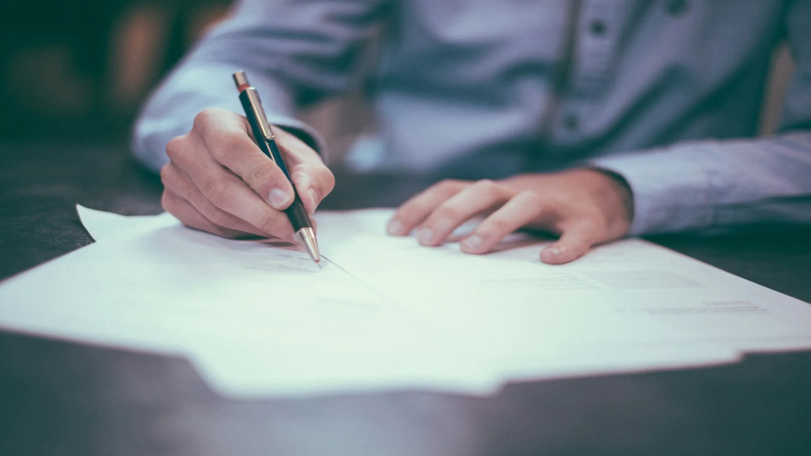 Persona firmando documentos en un escritorio